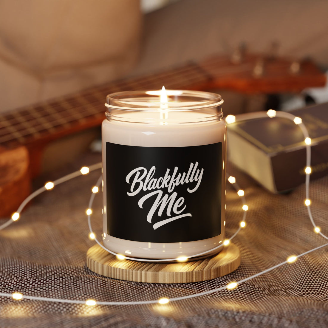 Candle in a jar labeled 'Blackfully Me' with a guitar and string lights in the background