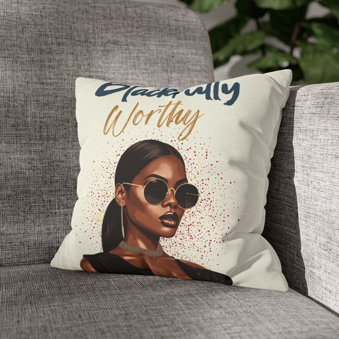 Pillow with a portrait of a woman wearing sunglasses and text 'Worthy' on a gray couch.